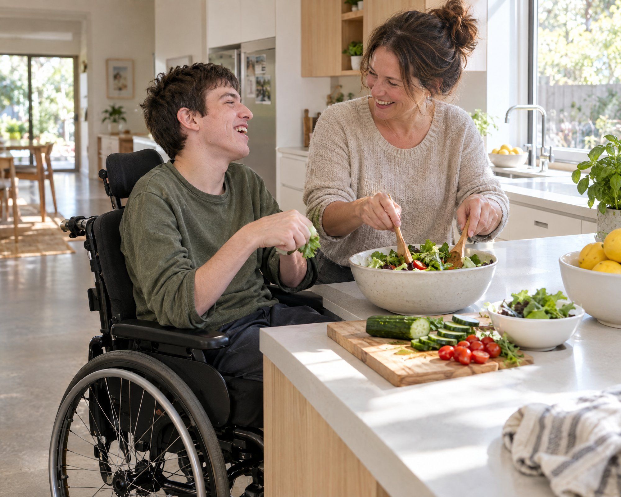A young man in a wheelchair and his support worker make a salad together at a lowered kitchen bench